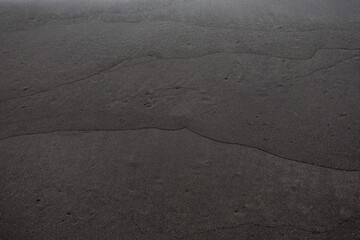 Smooth black volcanic sand with subtle wave-shaped lines, creating a minimal abstract texture useful for backgrounds or design purposes.