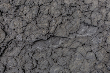 Detailed close-up of fractured volcanic stone surface with natural crevices and layered textures, ideal for geological themes or abstract design backgrounds