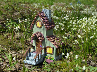 Cute fairy doll house with spring flowers outside in the garden. Lovely miniature for greeting cards, wedding or birthday concept, real estate, downsizing, home ownership. Vintage spring background