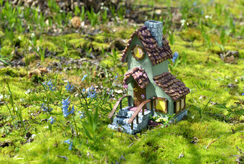 Cute fairy doll house with spring flowers outside in the garden. Lovely miniature for greeting cards, wedding or birthday concept, real estate, downsizing, home ownership. Vintage spring background