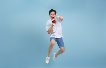 Energetic young man jumps while enthusiastically speaking into a megaphone against a light blue...