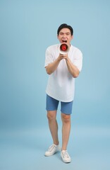 Young Asian man enthusiastically uses a megaphone while standing against a light blue background