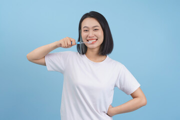 Smiling young woman brushing her teeth against a light blue background, promoting dental hygiene and wellness