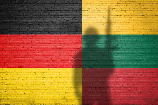 Germany and Lithuania flags painted on a brick wall with soldier shadow - Powered by Adobe