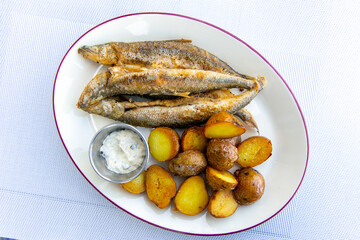 Fried smelt with boiled potatoes and mushroom sauce on a white plate. Delicious rustic lunch