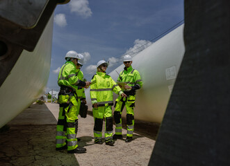 Maintenance engineer team standing at windmills at wind turbine farm. Group of people wear safety...