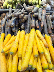 Assorted fresh vegetables on display at a local market, including black carrots, yellow carrots and green carrots. Colorful and neatly arranged root vegetables for sale