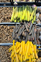 Assorted fresh vegetables on display at a local market, including turmeric, black carrots, yellow carrots and green carrots. Colorful and neatly arranged root vegetables for sale