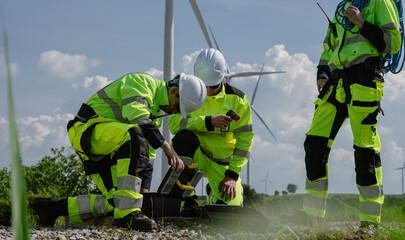 Maintenance engineer team standing at windmills at wind turbine farm. Group of people wear safety helmet and uniform working at alternative renewable energy wind station. Sustainable energy technology