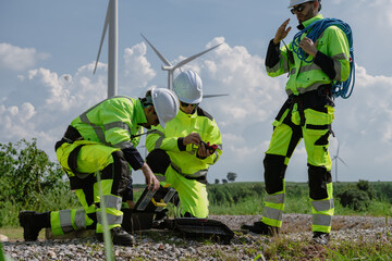 Maintenance engineer team standing at windmills at wind turbine farm. Group of people wear safety...