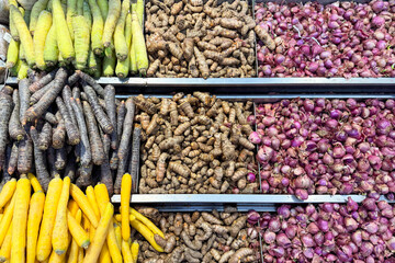 Assorted fresh vegetables on display at a local market, including turmeric, shallots, black carrots, yellow carrots and green carrots. Colorful and neatly arranged root vegetables for sale