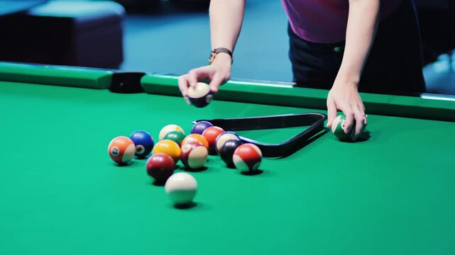 Hands placing colorful pool balls into triangle on a green felt billiards table
