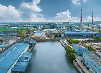 Industrial park with factory buildings alongside a waterway and a distant city skyline under a...