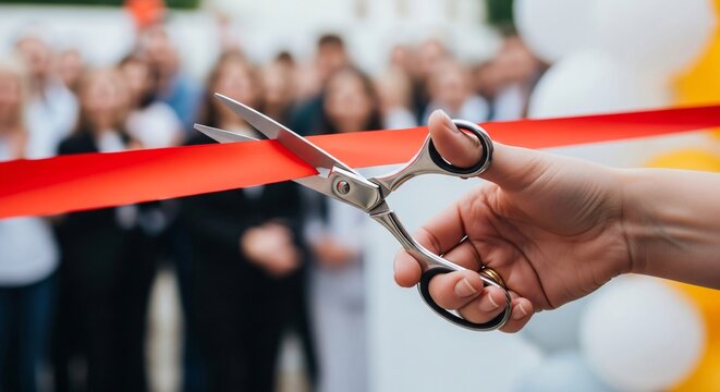 A hand cuts a red ribbon with scissors. The concept of opening a new business or for a grand opening ceremony.
