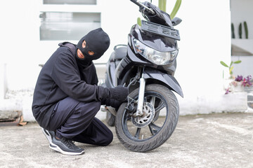 Masked Criminal in Balaclava Trying To Break Motorcycle Lock in a Parking Area.