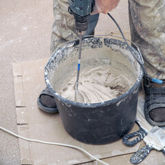 A worker stirs the construction mixture plaster in a bucket with an electric stirrer.