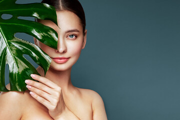Close up woman face with green exotic leaf. Skin care beauty treatments concept. Model with clean, health skin of face. Monstera Leaves © Oleg Gekman