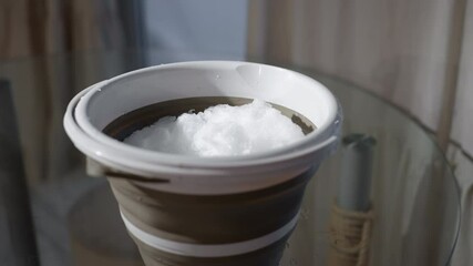 Collapsible bucket filled with fresh white snow sitting on glass table surface under soft window light water droplets glisten melting slowly capturing essence of winter indoors mood - Powered by Adobe
