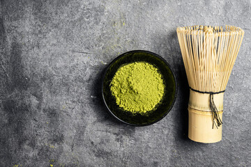 Matcha green tea powder in the black bowl and a traditional bamboo brush whisk or chasen on a black...