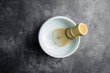Traditional bamboo brush whisk or chasen in an empty bowl on a black table. Accessories for making matcha green tea. Top view