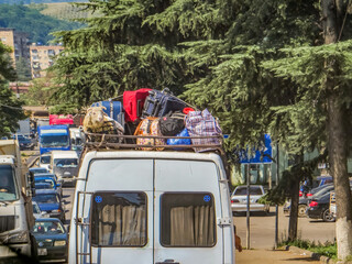 A van, packed high with luggage, including a bewildered-looking sheep, navigates a bustling street in Kutaisi, Georgia.