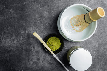 Matcha green tea powder in the black bowl with a wooden spoon and a traditional bamboo brush whisk...