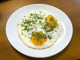 Fried eggs with chives and pepper on a white plate