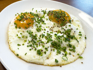 Sunny-side up eggs with chives and pepper on a white plate