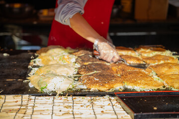 Chef is cooking Hiroshima Okonomiyaki at a food stall in Daisen Park. Osaka, Japan. Close up