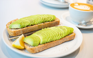 Top down view of two toast bread with sliced avocado topping and a cup of cappuccino. Tsuen Wan, Hong Kong. Selective focus, blurred background.