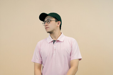 confident young man in casual pink shirt and green cap in casual and fashionable pose studio background