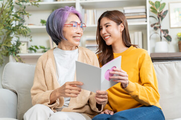 Smiling asian adult daughter greeting happy senior mother with mother's day presenting bouquet of flowers and card,happy elderly mom and grown up child hug embrace celebrate birthday at home together