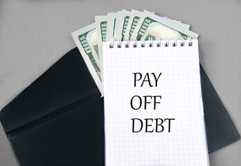 PAY OFF DEBT - words in a notebook against the background of a black envelope and banknotes