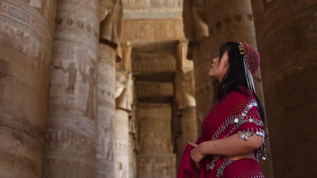 Woman in traditional outfit admires ancient columns at Dendera Temple in Egypt