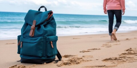A blue backpack rests on a sandy beach, with a person walking away into the distance, leaving footprints. Symbolizes travel, freedom, and seaside adventure.