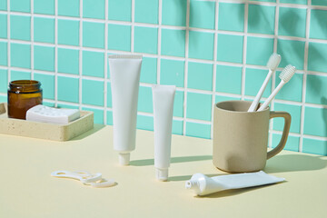 A cozy product scene with toothbrushes and toothpaste styled with wood and ceramic in front of mosaic green tiles. Warm and homey tone.