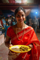 Joyful Bengali Woman Offering Prashad During Kali Puja Celebration in Traditional Red Saree.