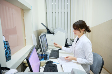 Young female doctor radiologist doing CT or MRI scan in clinic. Remote control of the CT scanner. A...