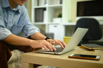 Close up of man working on laptop at home, focusing on hands typing on keyboard