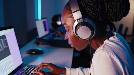 Focused black female developer coding on laptop in modern office at night - Powered by Adobe