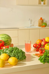 Lots of fresh vegetables are placed on the kitchen island in the modern kitchen space. Fresh lemons, tomatoes, apples and watermelon... In the middle is a glass of delicious juice and space for design