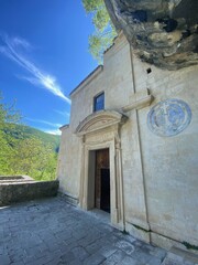 Fototapeta premium Stone hermitage nestled against rocky cliff, weathered walls framing wooden door, providing spiritual sanctuary within Majella National Park's serene landscape in Abruzzo region