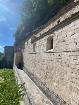 Stone pathway winding beside ancient wall, revealing Santo Spirito a Majella Hermitage nestled within tranquil Abruzzo landscape, embodying historical spiritual sanctuary