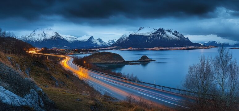 Coastal highway at twilight, light trails streak along a winding road beside a tranquil fjord, snow-capped mountains in the background under a dramatic sky - Powered by Adobe