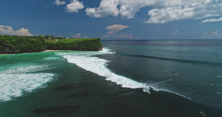 Stunning aerial drone footage capturing surfers riding perfect waves at the famous Dreamland Beach in Bali, Indonesia, showcasing the vibrant turquoise waters and lush green cliffs