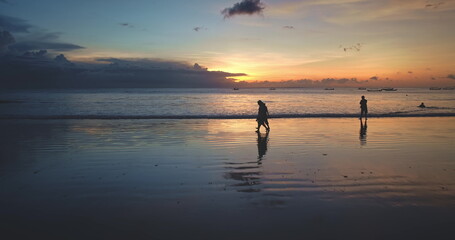 Tourists walking along Dreamland Beach in Bali, Indonesia, during a vibrant sunset, soaking in the stunning scenery and tranquil ocean waves, creating a perfect evening atmosphere