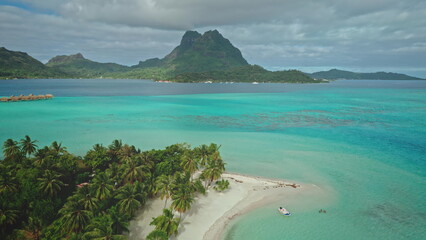 Turquoise lagoon water gently laps the idyllic white sand beach of Bora Bora, with mount Otemanu...