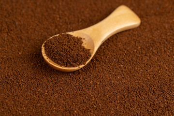 ground coffee and a wooden spoon, a large number of roasted ground coffee beans in powder and a wooden spoon, closeup
