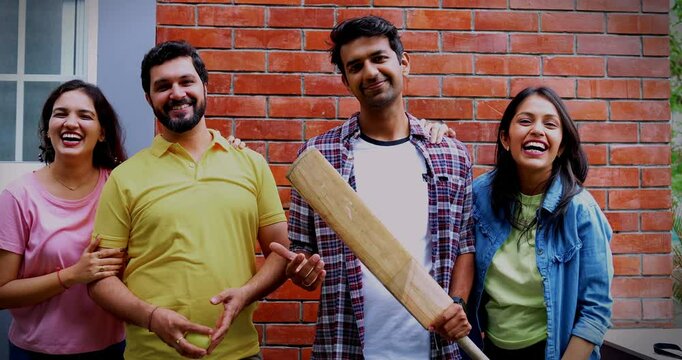College team with bat ball posing together, Indian Asian university students smiling confidently as male and female cricket players hold bat and ball while standing against red brick campus wall