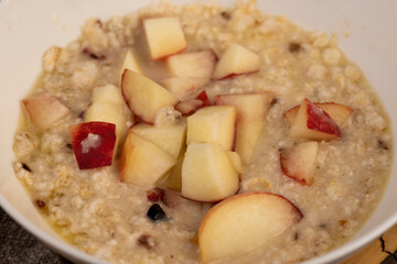adding pieces of peach to hot oatmeal , quickly cooked oatmeal porridge with dried fruits and...